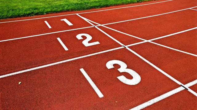 The start of a red running track, with white lines and the lane numbers 1, 2 and 3 painted on it.