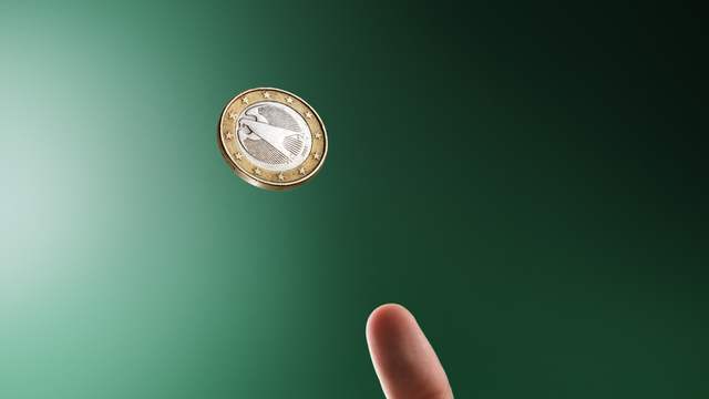 A coin spinning in the air above a hand with the thumb raised, against a green background.