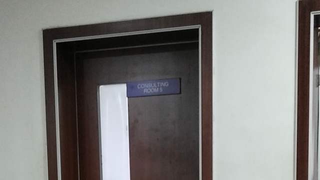 A closed wooden door in a clinic corridor with a small sign that reads Consulting Room 5.