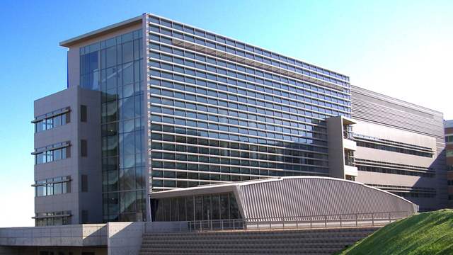 A modern office and laboratory building with a glass front and long rows of windows, under a clear blue sky.