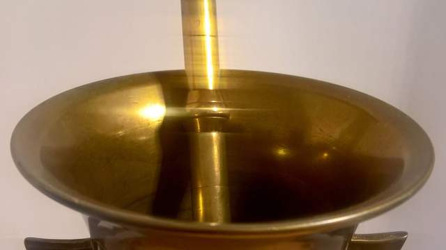 An old brass mortar with two handles and a heavy brass pestle standing in it.