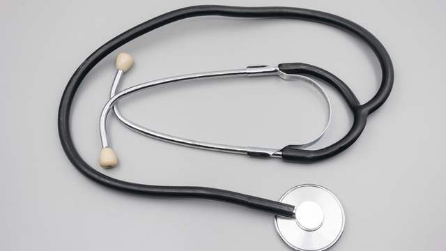 A stethoscope with black tubing and a silver chest piece lying on a plain grey surface.
